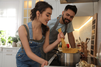 Photo of Lovely young couple cooking pasta together in kitchen