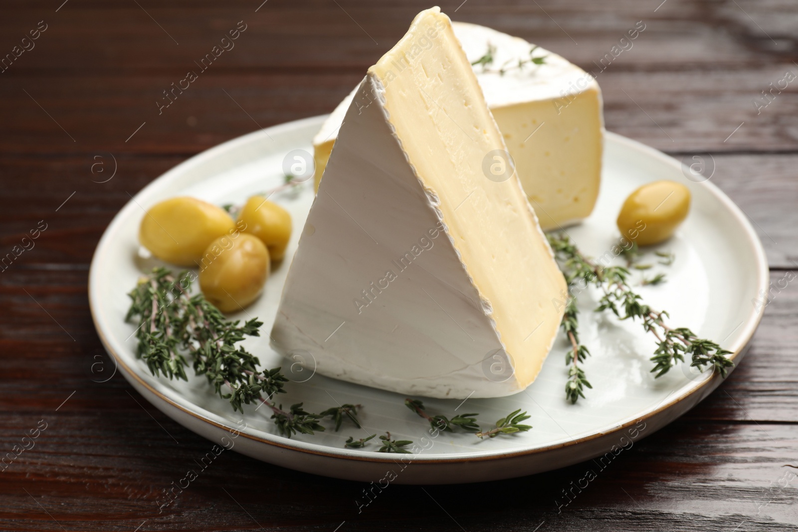 Photo of Plate with pieces of tasty camembert cheese, olives and rosemary on wooden table, closeup