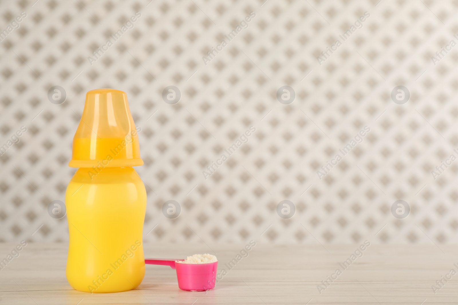 Photo of Feeding bottle with infant formula and scoop of powder on white wooden table, space for text. Baby milk