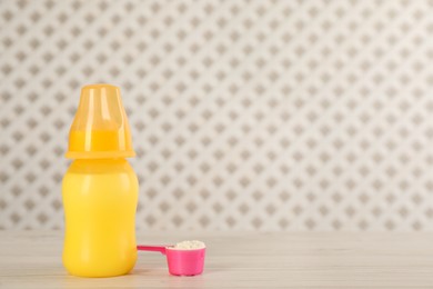 Feeding bottle with infant formula and scoop of powder on white wooden table, space for text. Baby milk