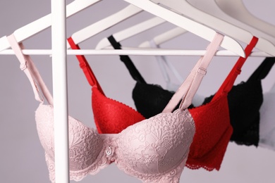 Photo of Hangers with beautiful lace bras on rack against grey background. Stylish underwear