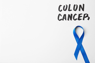 Photo of Blue awareness ribbon and words COLON CANCER on white background, top view