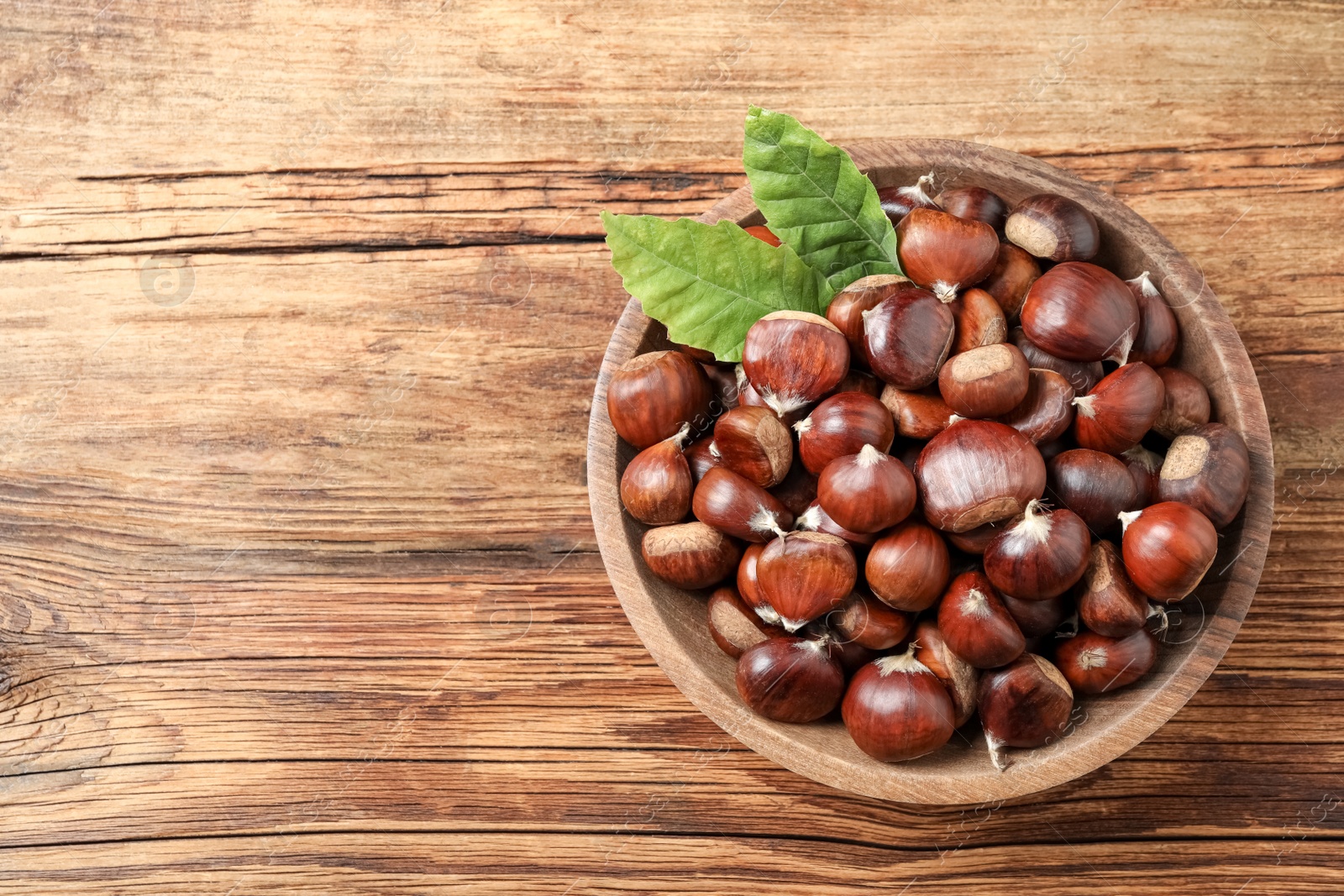 Photo of Fresh sweet edible chestnuts in bowl on wooden table, top view. Space for text