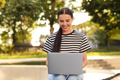 Photo of Happy young woman using modern laptop outdoors