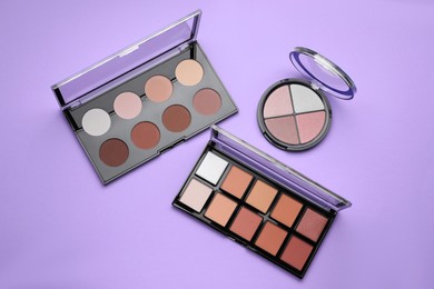 Photo of Colorful contouring palettes on violet background, flat lay. Professional cosmetic product