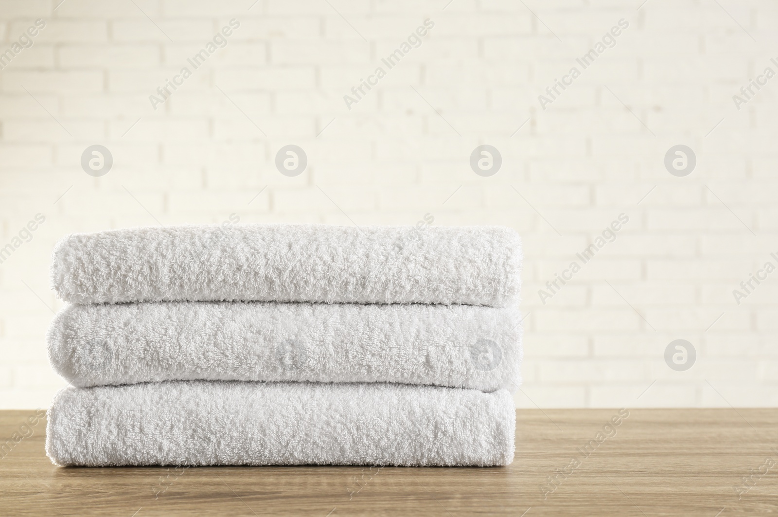 Photo of Stack of clean bath towels on wooden table near white brick wall