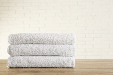 Stack of clean bath towels on wooden table near white brick wall