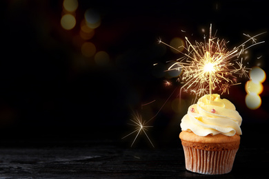 Image of Birthday cupcake with sparkler on table against dark background. Space for text
