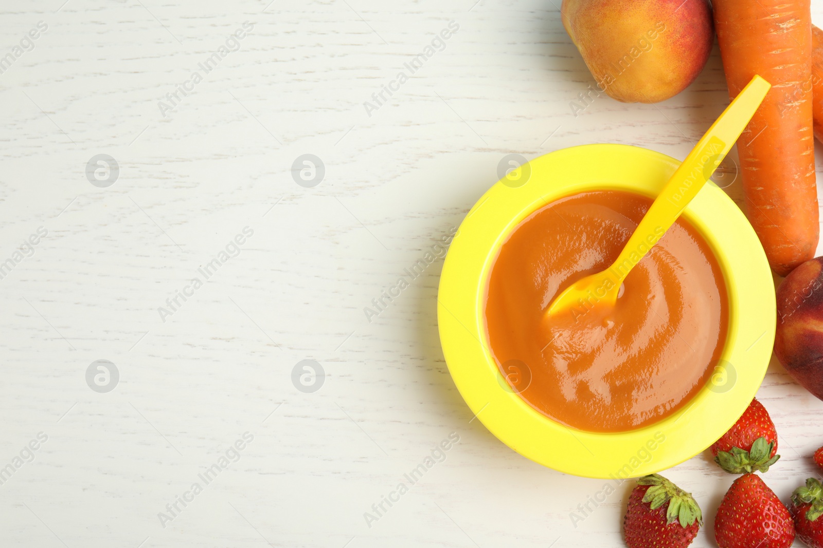 Photo of Baby food in bowl and fresh ingredients on white wooden table, flat lay. Space for text