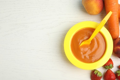 Baby food in bowl and fresh ingredients on white wooden table, flat lay. Space for text