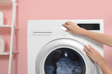 Woman putting laundry into washing machine indoors, closeup