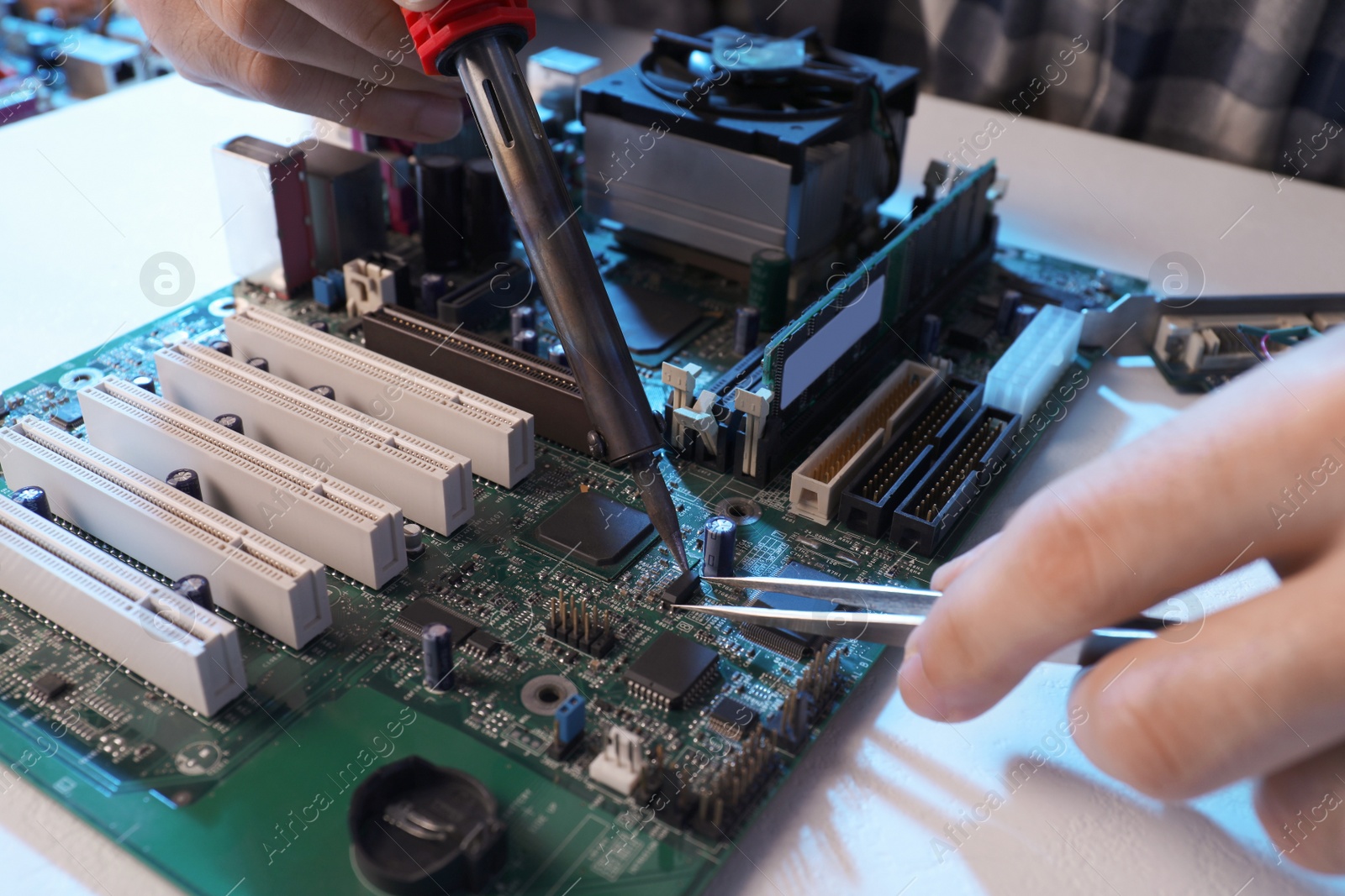 Photo of Technician repairing electronic circuit board with soldering iron at table, closeup