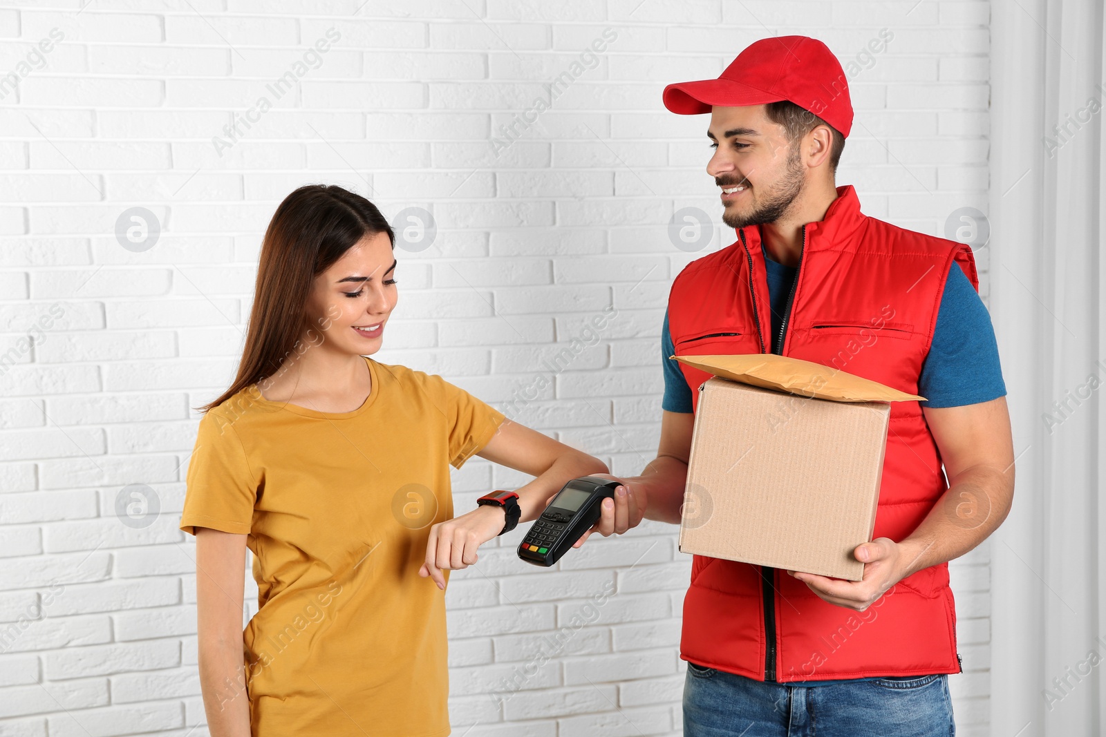 Photo of Young woman with smartwatch using terminal for delivery payment indoors