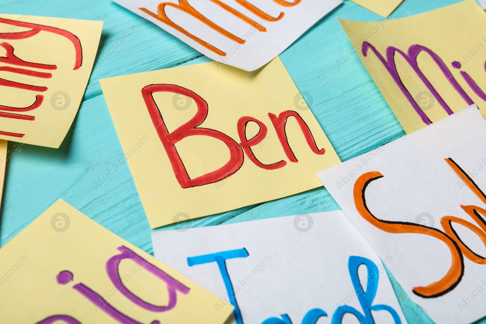 Photo of Paper notes with different baby names on light blue wooden table, closeup