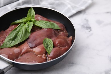 Raw chicken liver with basil in frying pan on white marble table, closeup