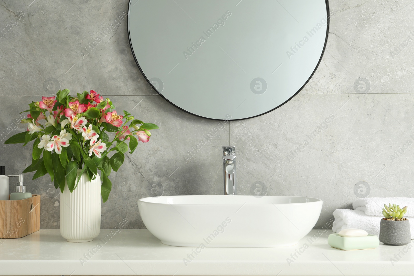 Photo of Vase with beautiful Alstroemeria flowers and toiletries near sink in bathroom