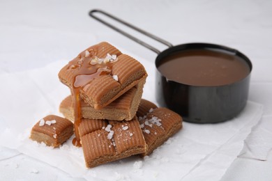 Yummy caramel candies, sauce and sea salt on white table, closeup