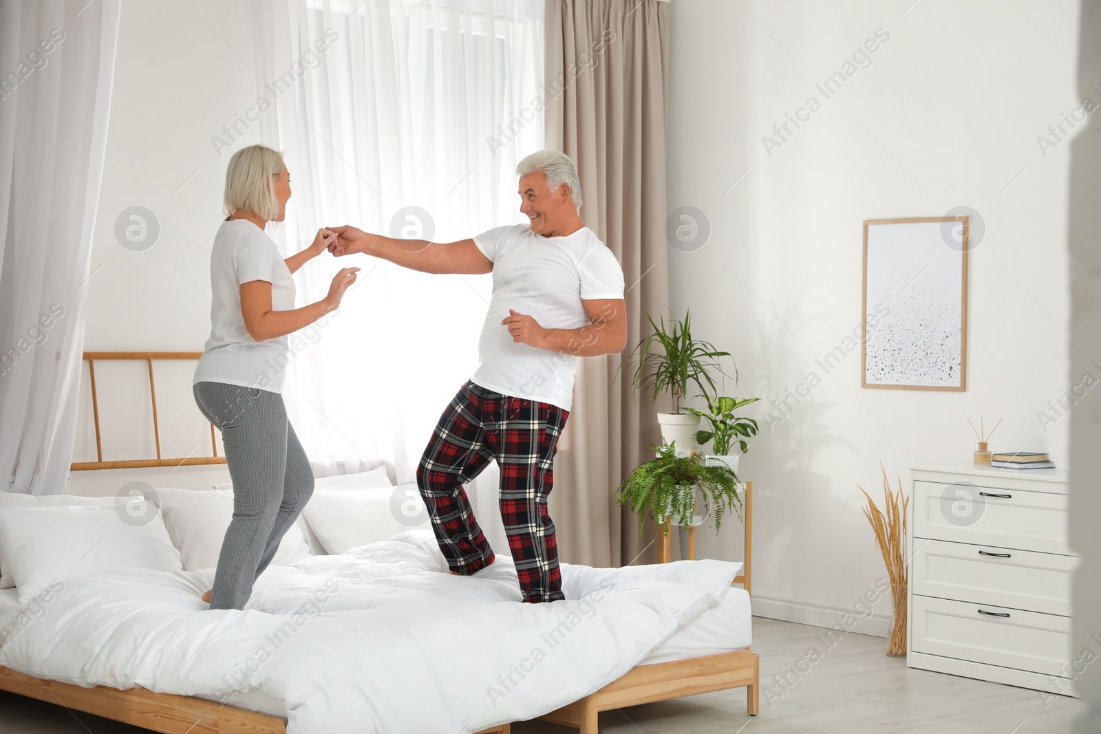 Photo of Happy mature couple dancing together on bed at home