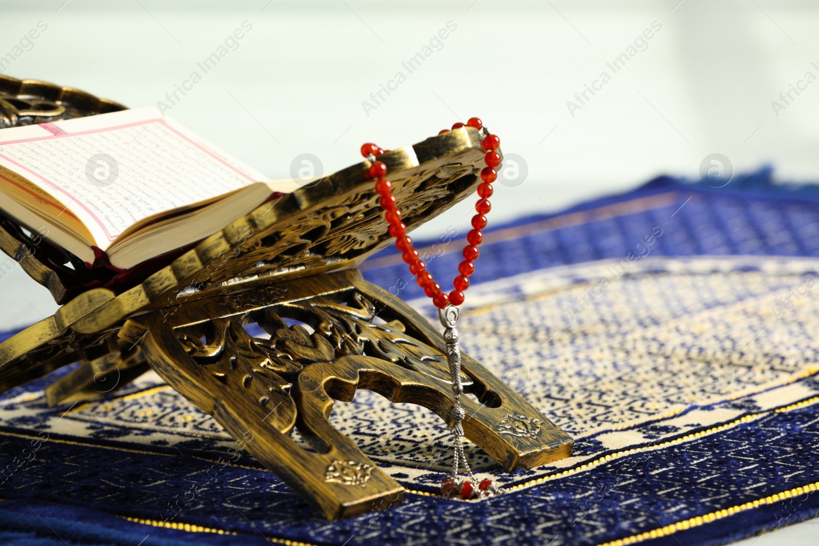 Photo of Rehal with open Quran and Misbaha on Muslim prayer rug, closeup