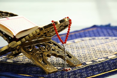 Rehal with open Quran and Misbaha on Muslim prayer rug, closeup