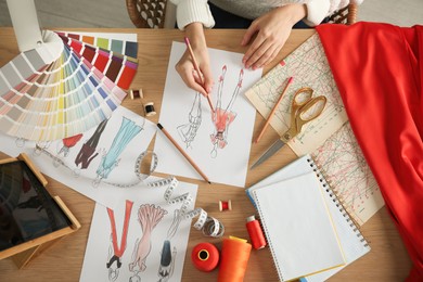 Photo of Fashion designer creating new clothes in sketchbook at wooden table, top view