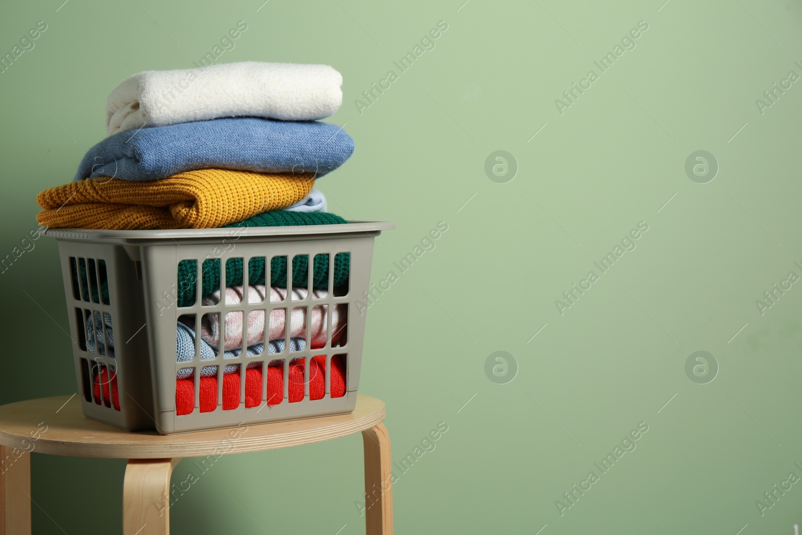 Photo of Plastic laundry basket with clean clothes on wooden table near light green wall. Space for text
