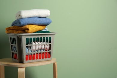 Plastic laundry basket with clean clothes on wooden table near light green wall. Space for text
