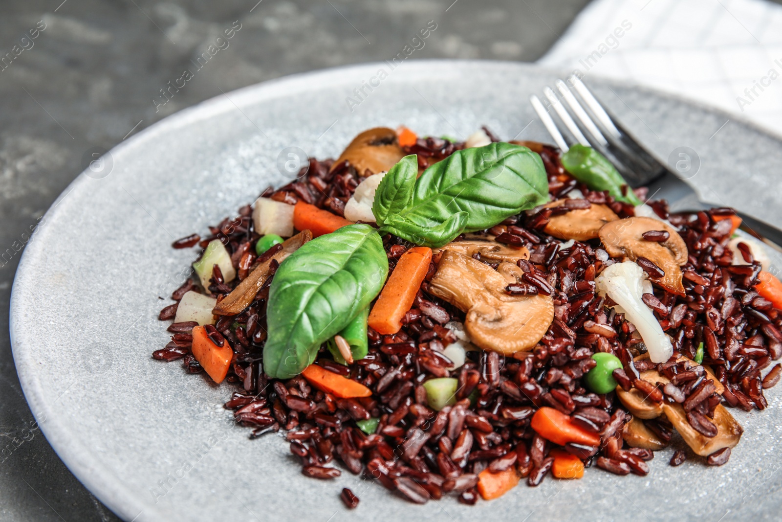 Photo of Plate of brown rice with vegetables on table, closeup