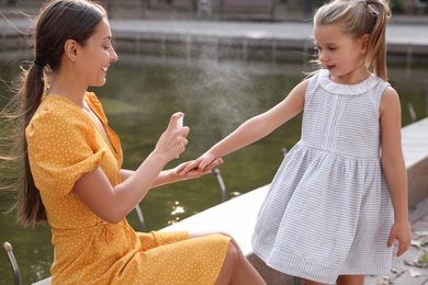 Mother applying insect repellent onto girl's hand outdoors