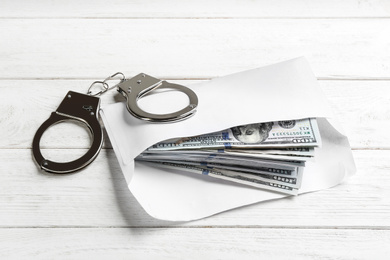 Dollar bills and handcuffs on white wooden table. Bribe concept