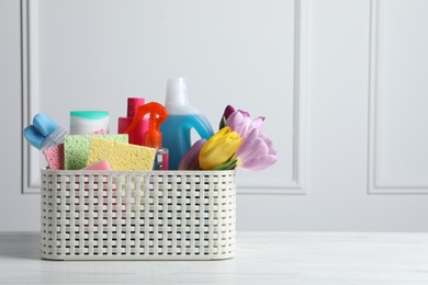 Spring cleaning. Basket with detergents, flowers and tools on white wooden table. Space for text