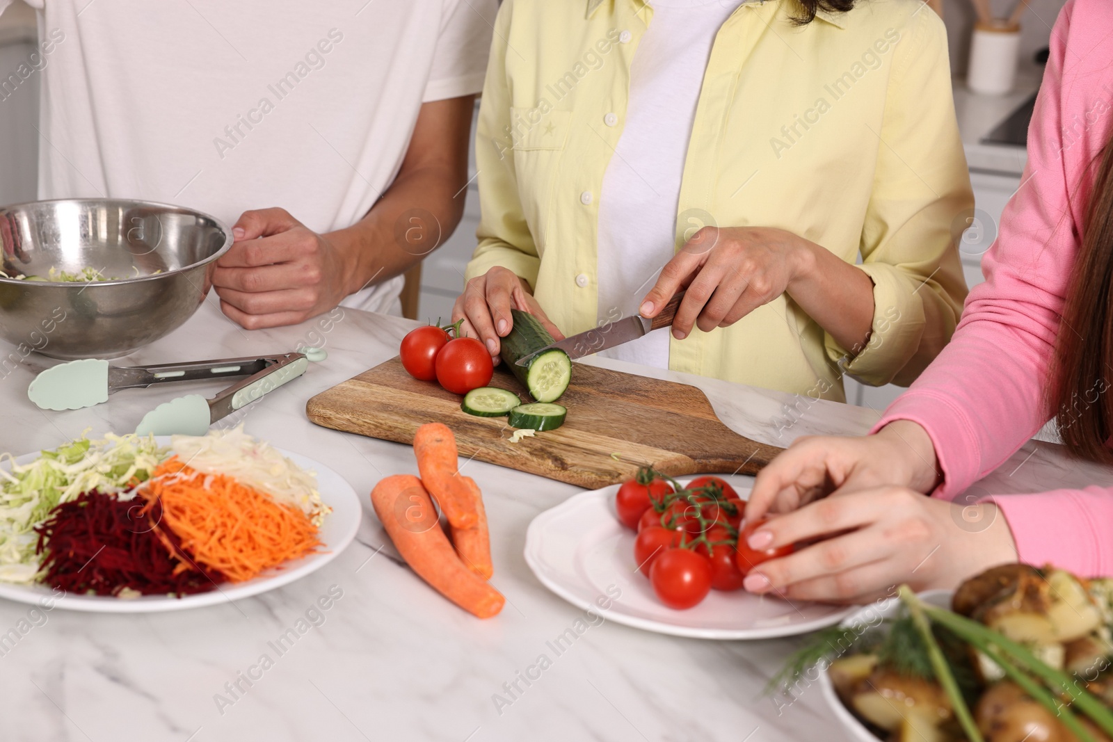 Photo of Friends cooking healthy vegetarian meal at white marble table in kitchen, closeup