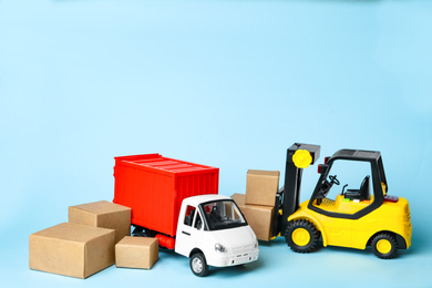 Photo of Different toy vehicles with boxes on blue background. Logistics and wholesale concept