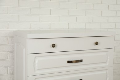 Photo of Modern chest of drawers near white brick wall