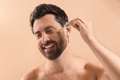 Photo of Smiling man applying cosmetic serum onto his face on beige background