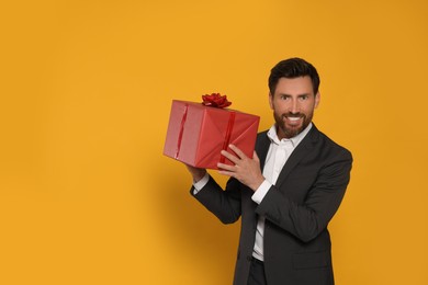 Handsome man holding gift box on yellow background, space for text