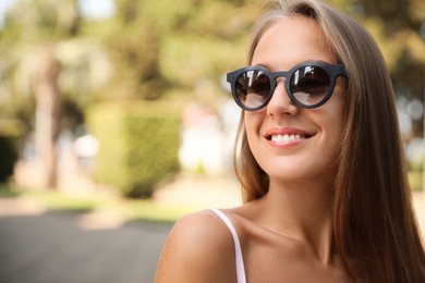 Photo of Beautiful young woman in stylish sunglasses outdoors, space for text