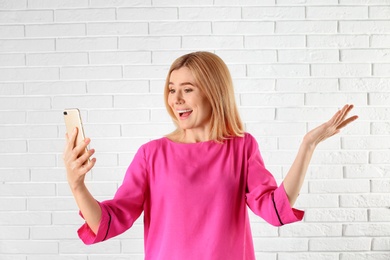 Photo of Woman using mobile phone for video chat against brick wall