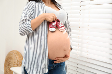 Photo of Pregnant woman with cute baby shoes at home, closeup