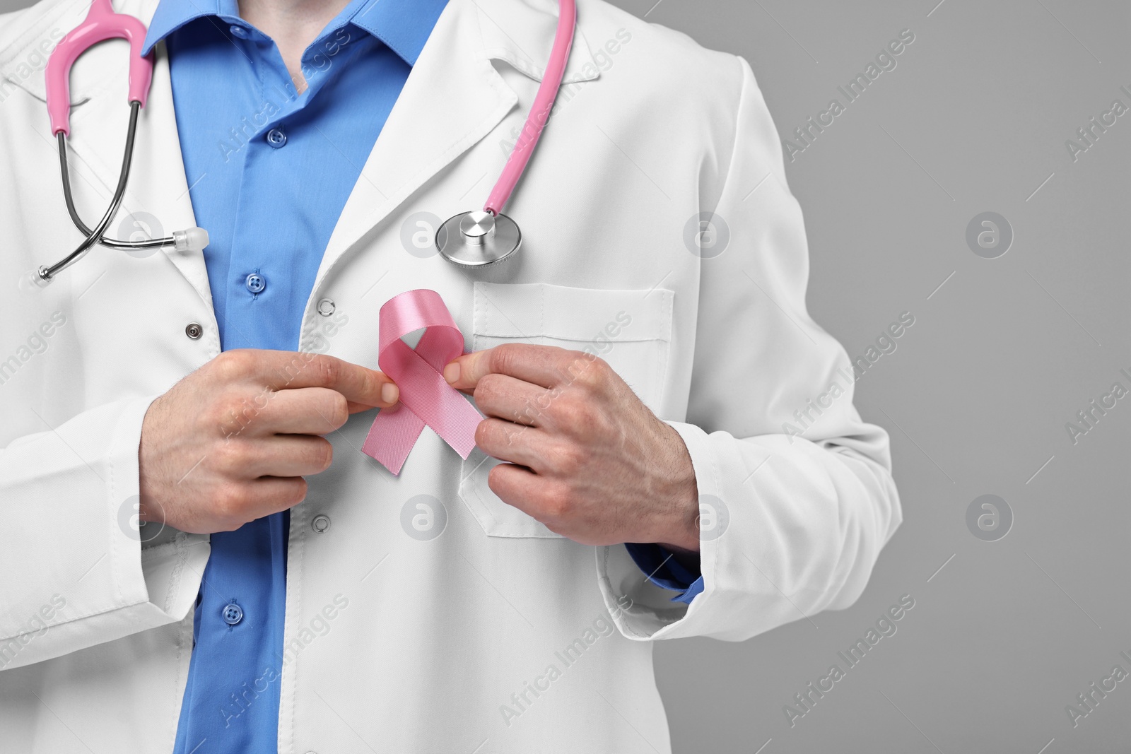 Photo of Mammologist with pink ribbon and stethoscope on grey background, closeup. Space for text