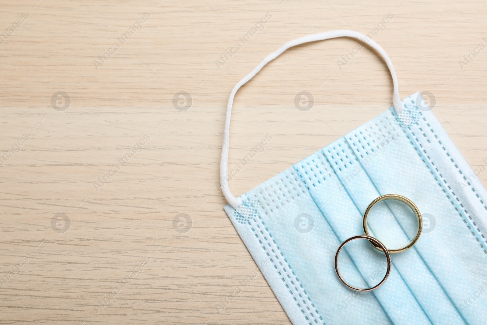 Photo of Protective mask and wedding rings on wooden table, flat lay with space for text. Divorce during coronavirus quarantine