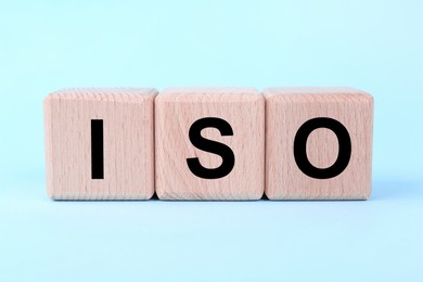 Photo of International Organization for Standardization. Wooden cubes with abbreviation ISO on light blue background, closeup