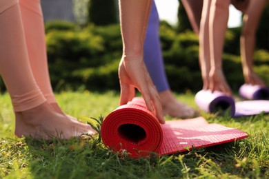 Women rolling yoga mats outdoors on sunny day, closeup