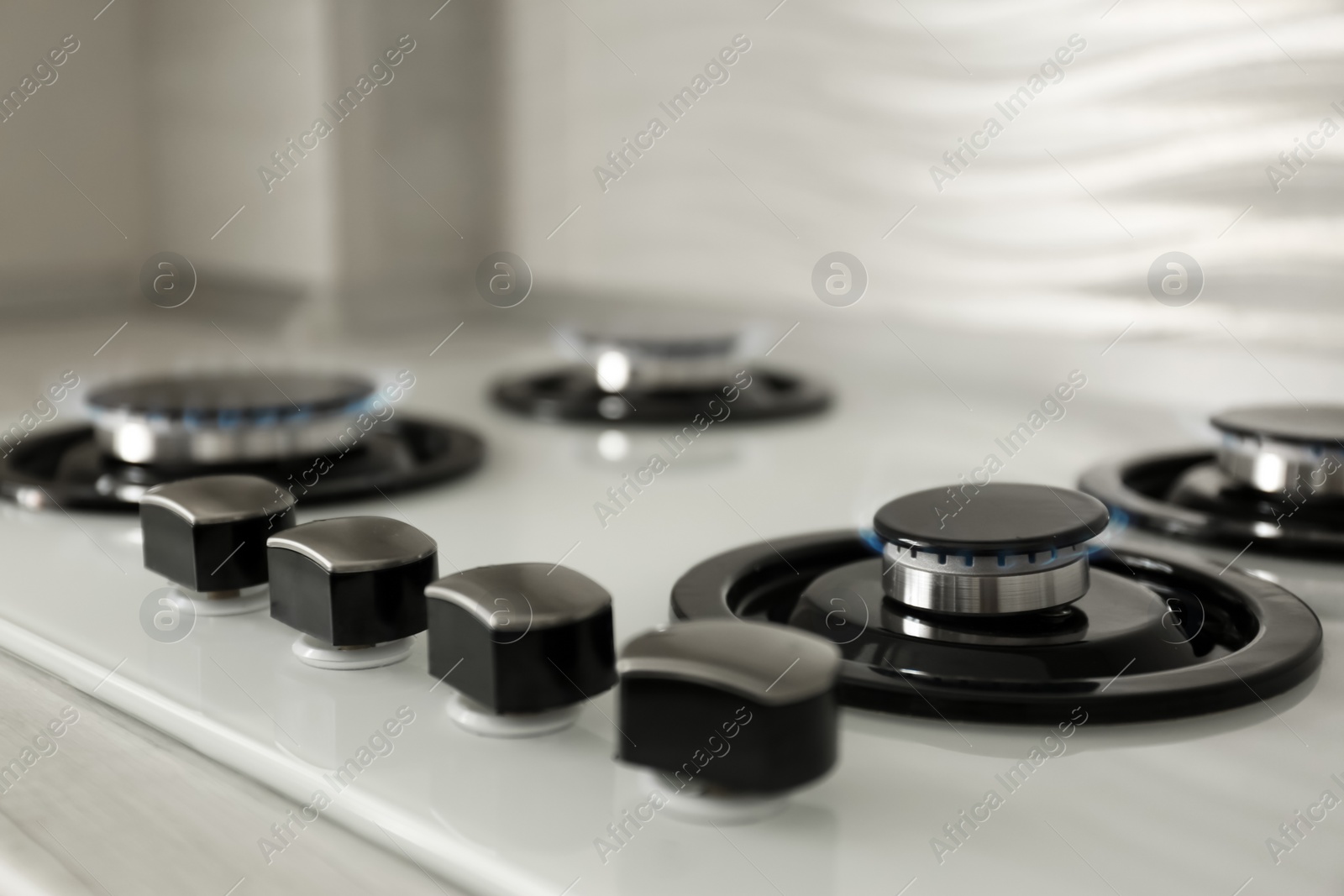 Photo of Gas burners with blue flame on modern stove, closeup