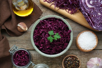 Photo of Tasty red cabbage sauerkraut with parsley and different ingredients on wooden table, flat lay