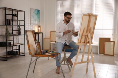 Photo of Young man painting on easel with brush in artist studio