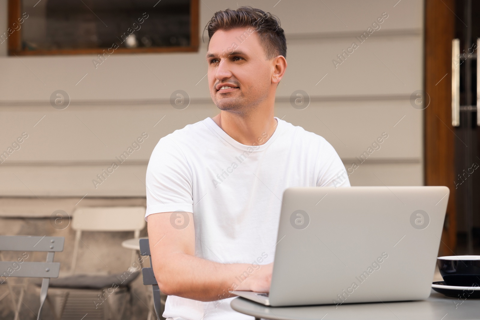 Photo of Handsome man working on laptop at table in outdoor cafe