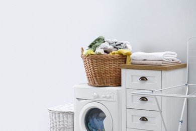 Photo of Wicker basket with dirty laundry on washing machine indoors