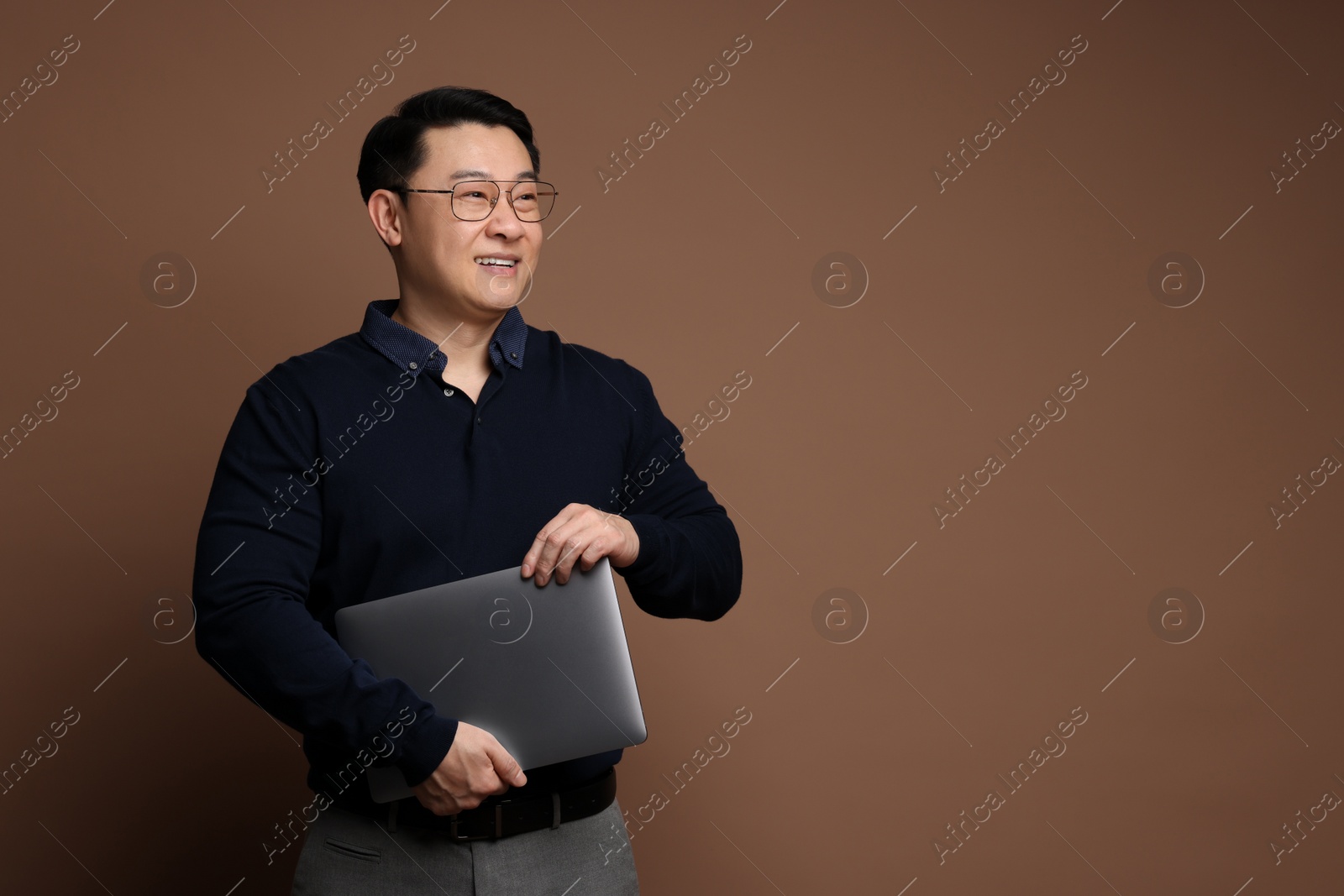 Photo of Portrait of happy man with laptop on brown background. Space for text