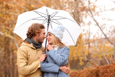 Photo of Young romantic couple with umbrella in park on autumn day